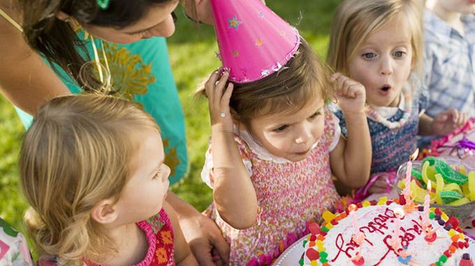 Girl in party hat blowing candles on cake